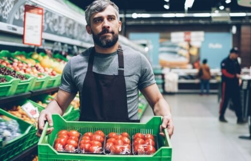 HEB interview questions prep: a grocery worker carrying a crate of tomatoes through the produce aisle