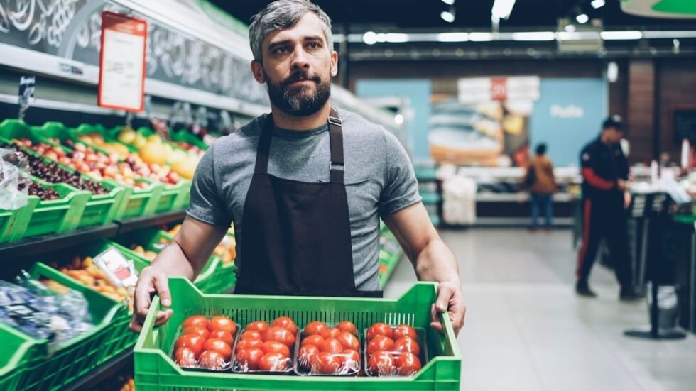 HEB interview questions prep: a grocery worker carrying a crate of tomatoes through the produce aisle