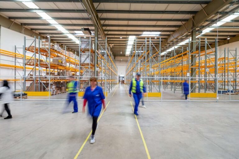Amazon seasonal jobs: warehouse associates in safety vests walking an aisle between tall storage racks